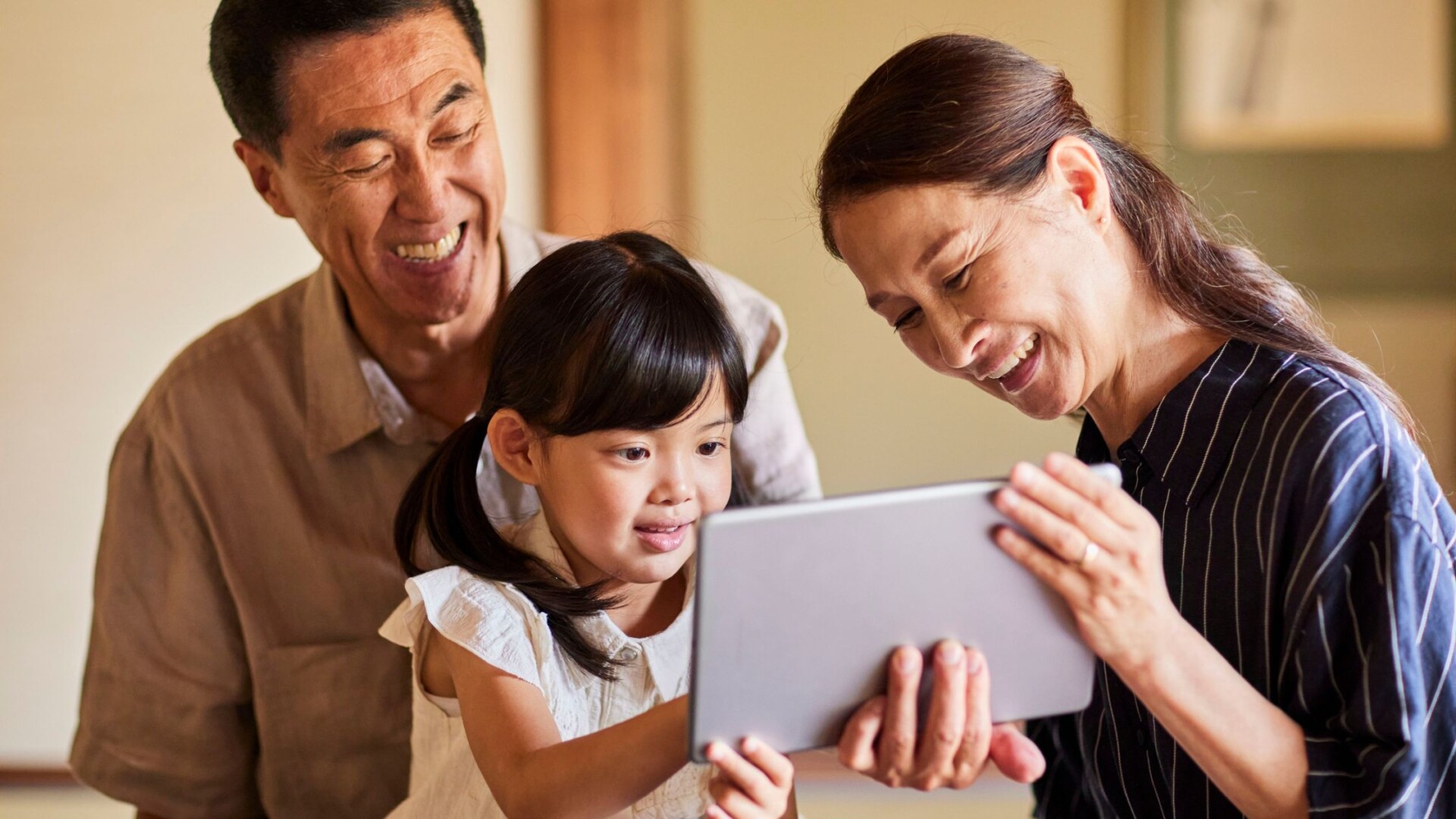 Grandparents guiding their grandchild on a tablet, learning about money habits and financial wellness.