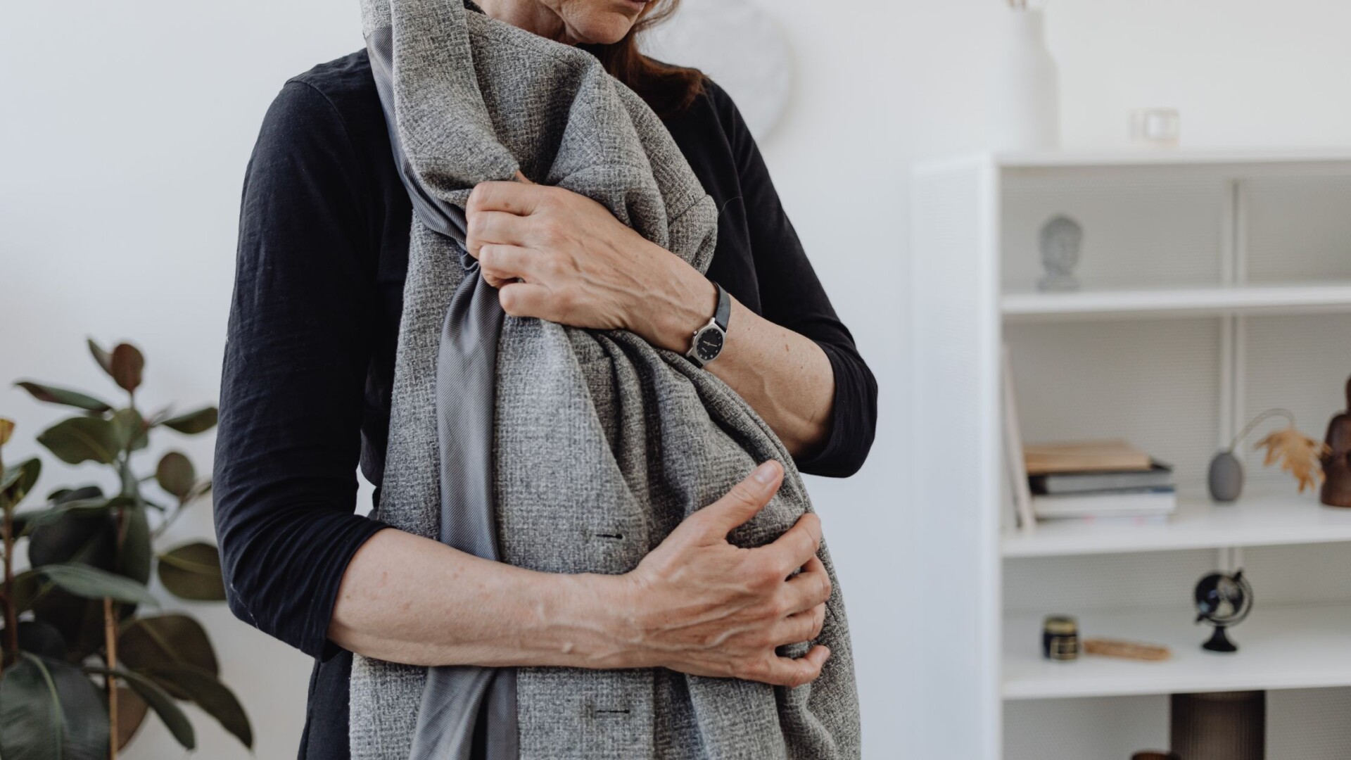 Woman holding husbands coat at home reflecting, representing emotional healing and self care after loss