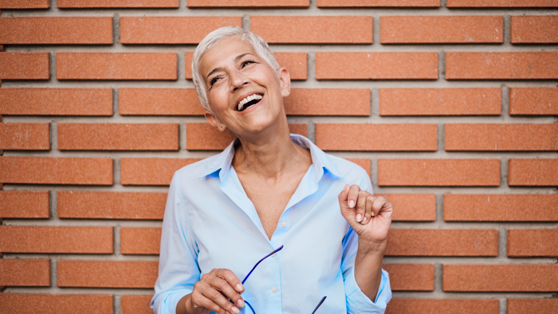 Woman smiling confidently while standing in front of a textured brick wall, representing strength, resilience, and positive mindset